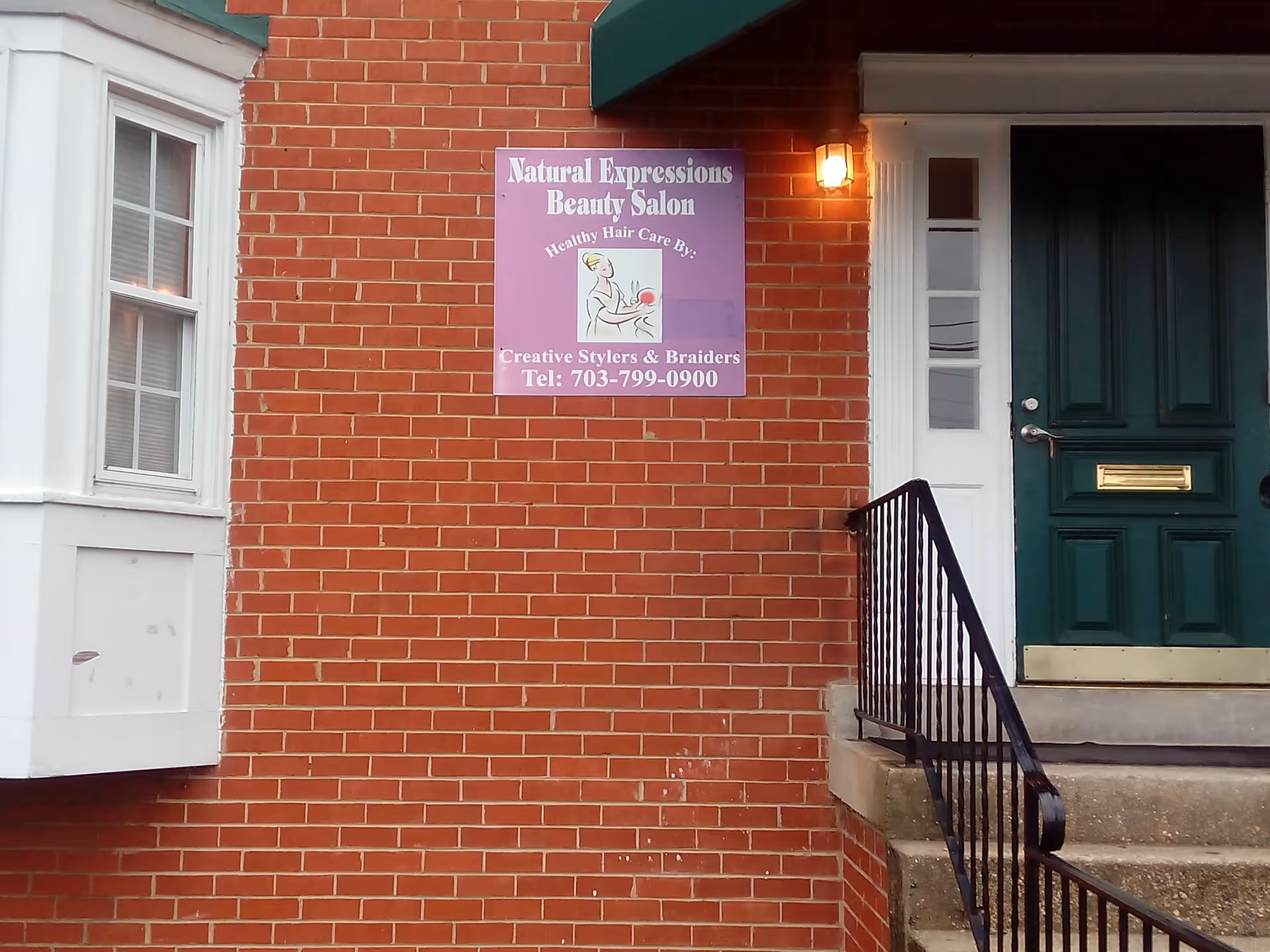 A brick exterior wall with a purple Natural Expressions Beauty Salon sign beside a green door.
