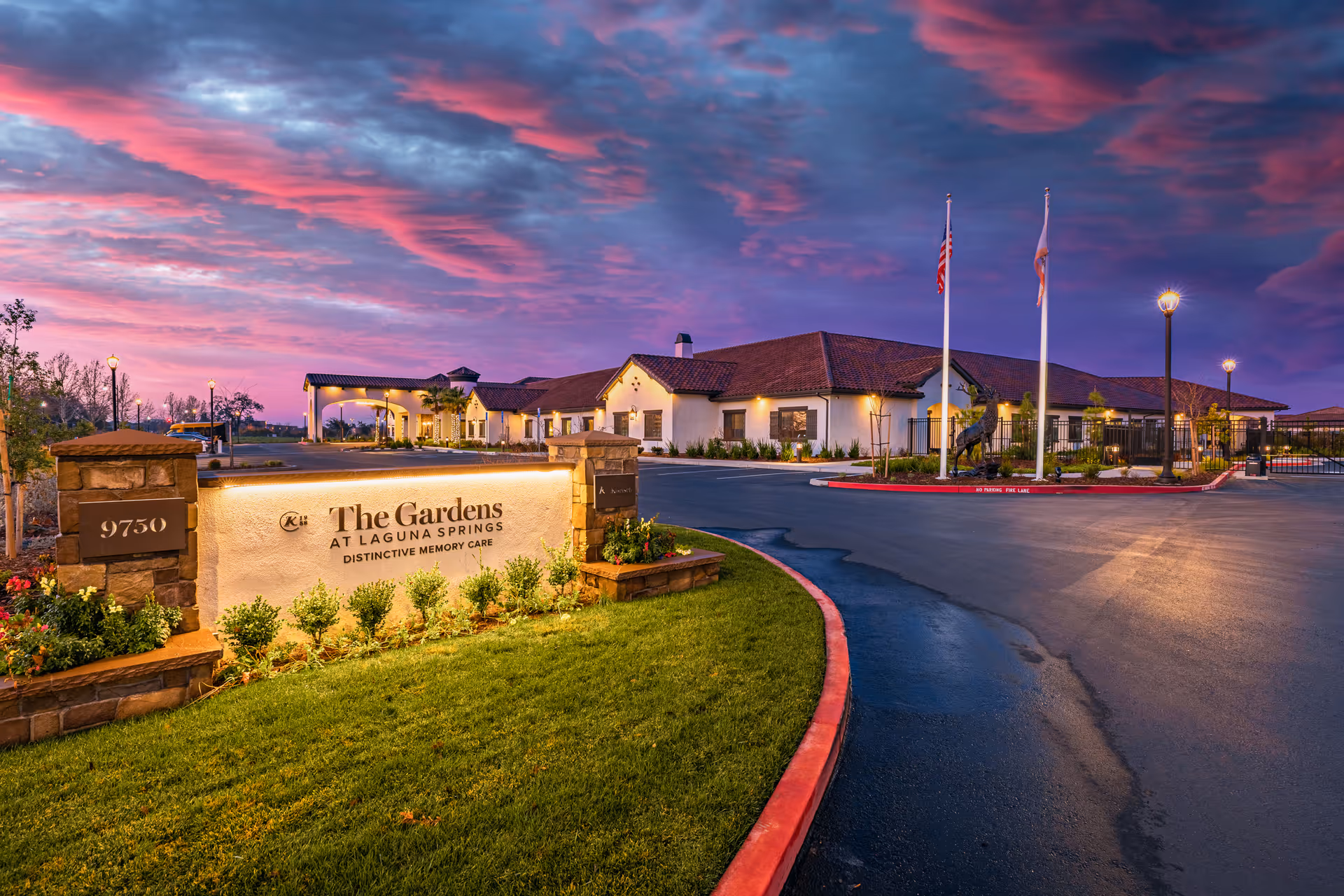 Exterior view of The Gardens at Laguna Springs entrance with sign, driveway, and sunset sky.