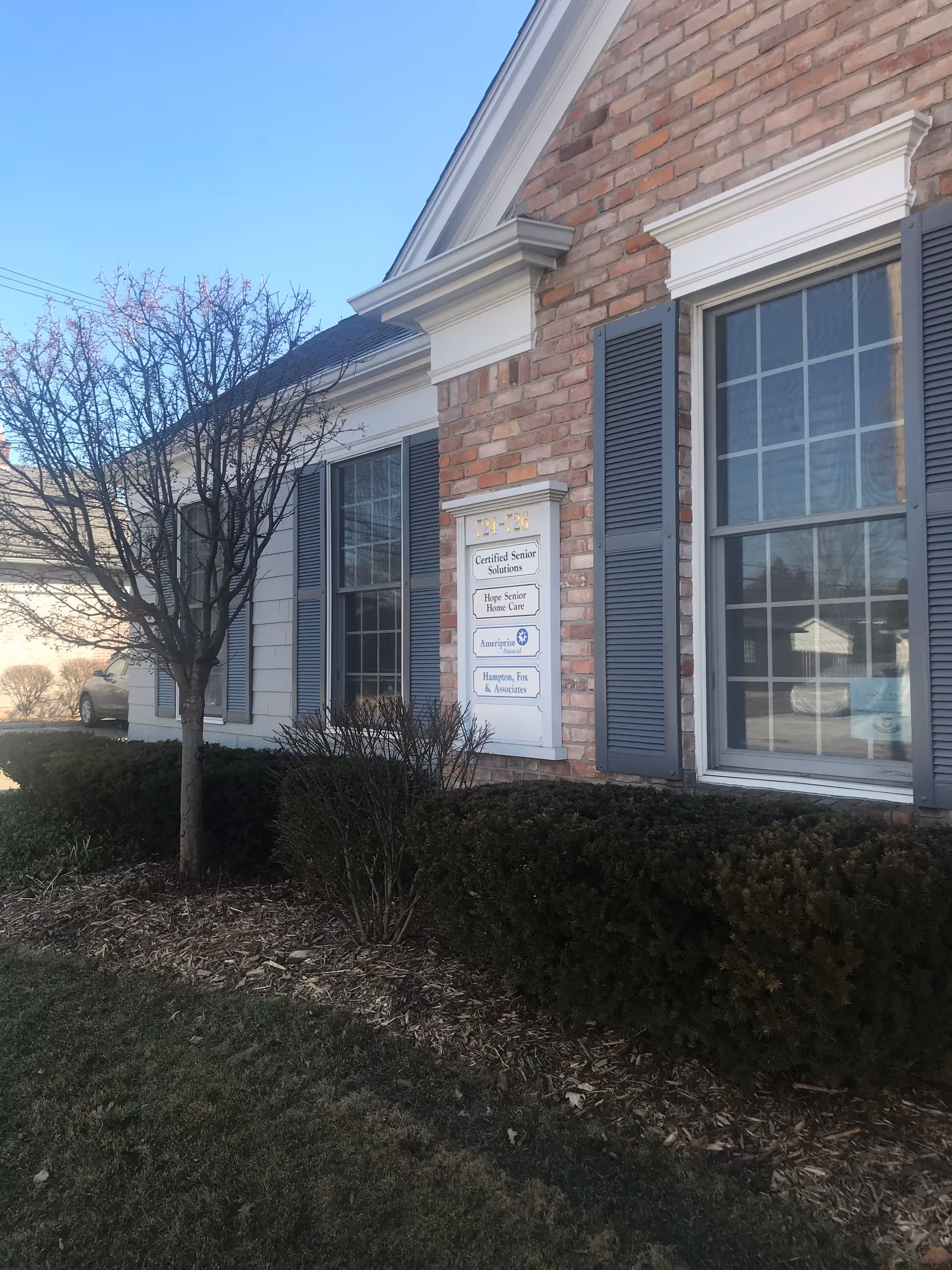 Brick senior living facility exterior with large windows, shutters, and a sign by the entrance.