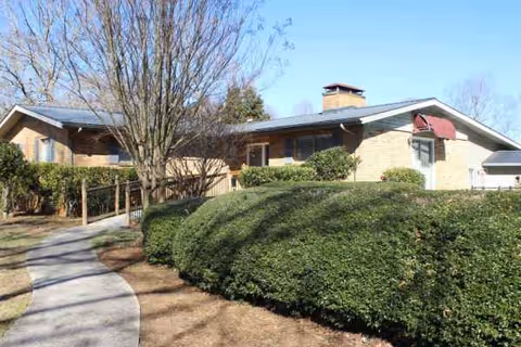 Front exterior of a single-story brick senior living facility with a walkway and trimmed hedges.