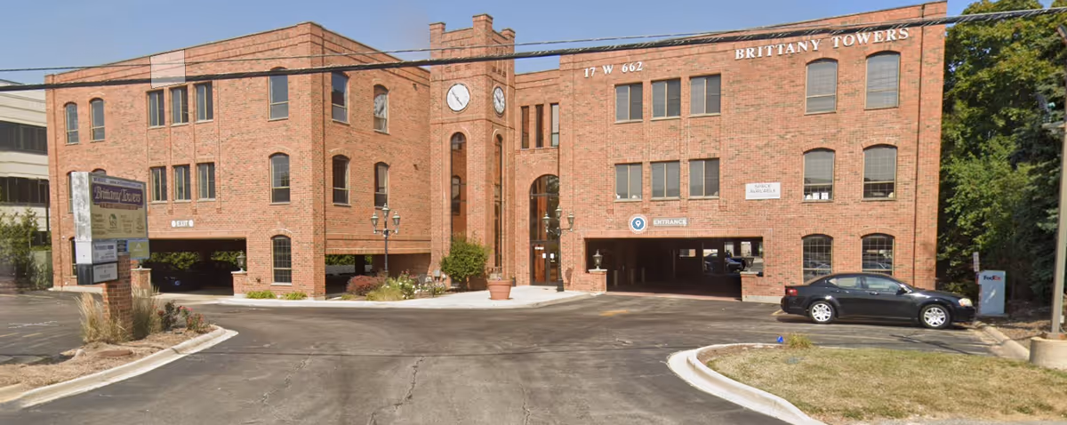 Exterior brick building with central archway and driveway, labeled Brittany Towers.