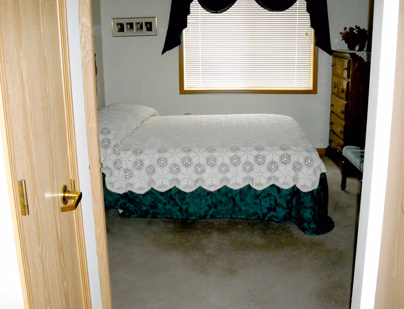 A small bedroom with a bed, window, dresser, and chair.