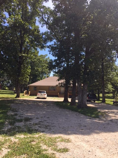 A single-story building with a driveway and several parked cars surrounded by trees.