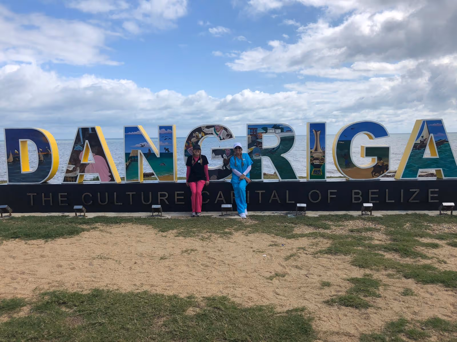 Outdoor scene with a large Dangriga sign and two people posing.