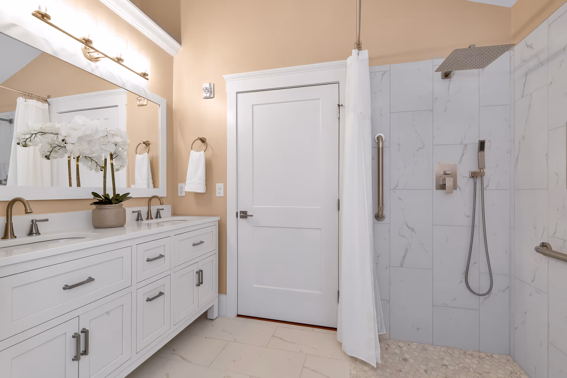 Bright bathroom with double vanity, marble shower, and white towels in a residential space.