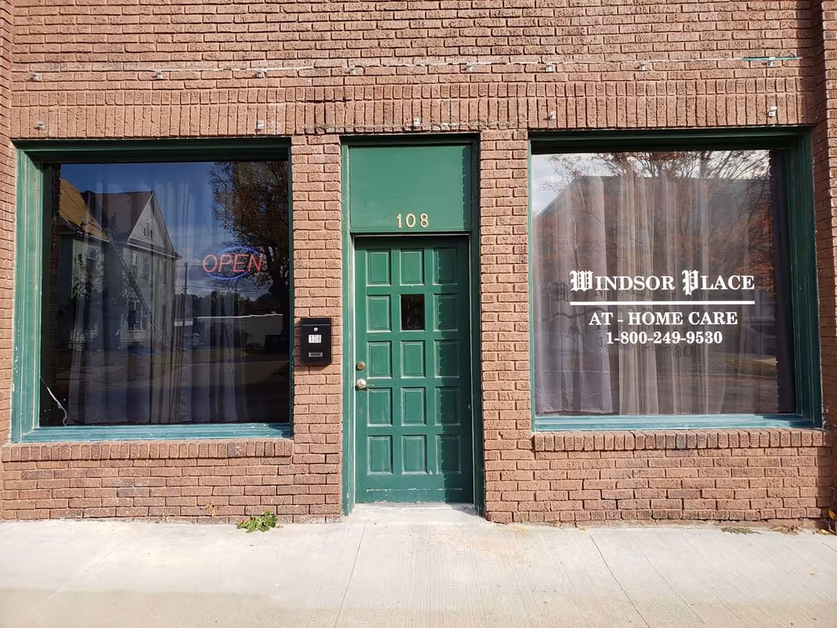 Brick building front with green door and two large windows displaying Windsor Place At Home Care.