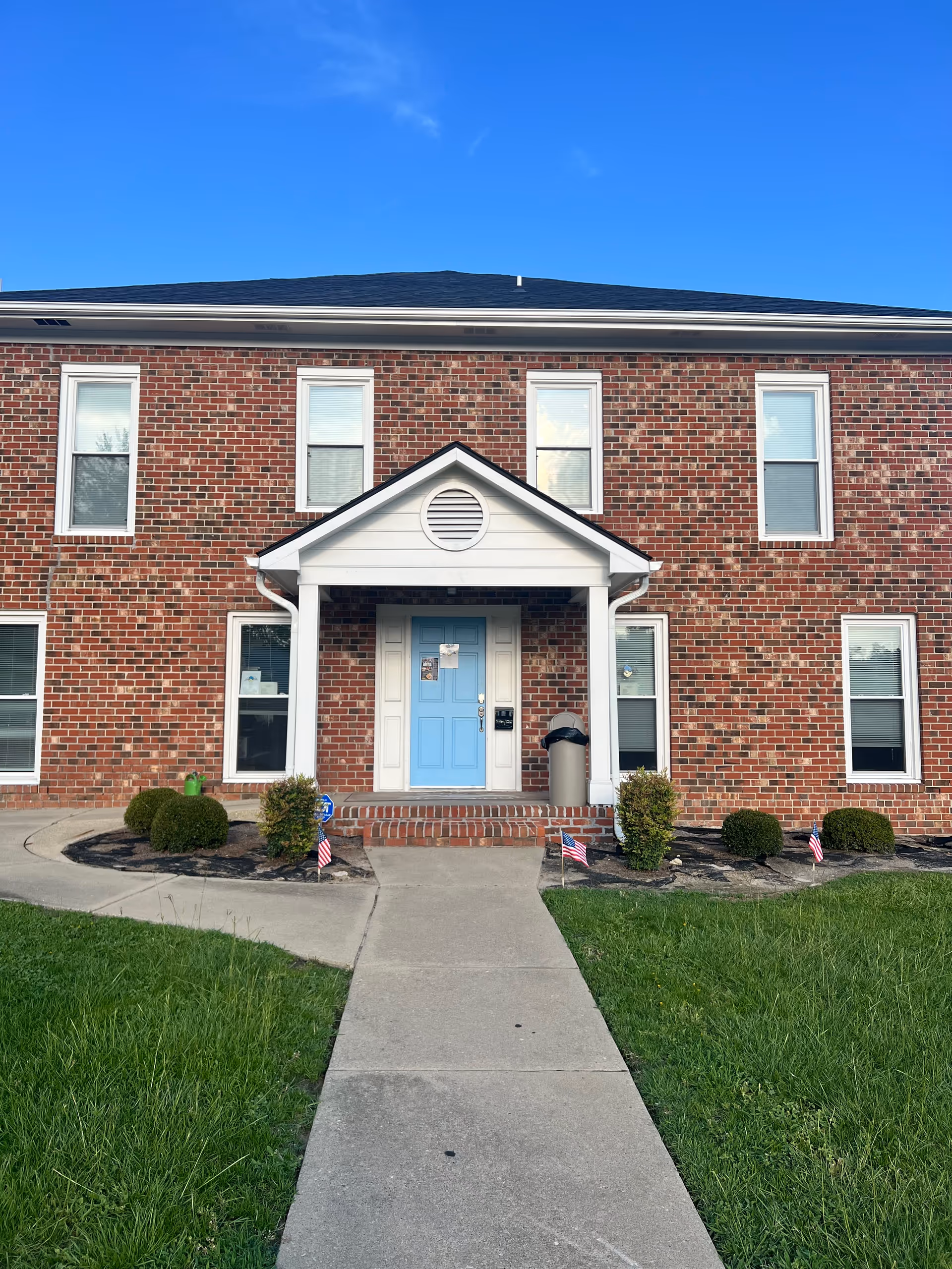 Brick senior living facility entrance with blue door and landscaped walkway.