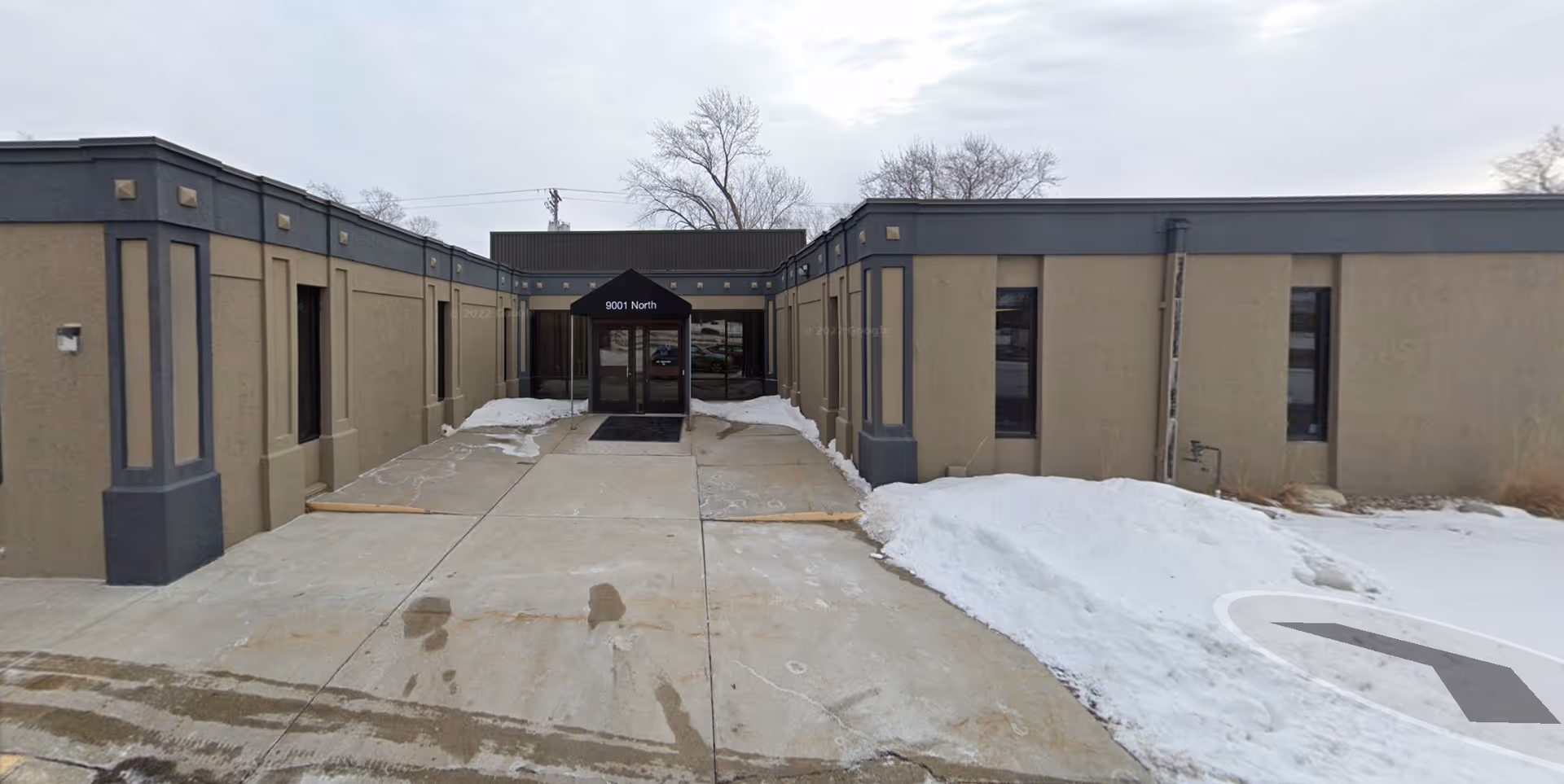 A beige, single story facility exterior with a central entrance and snowy pavement.
