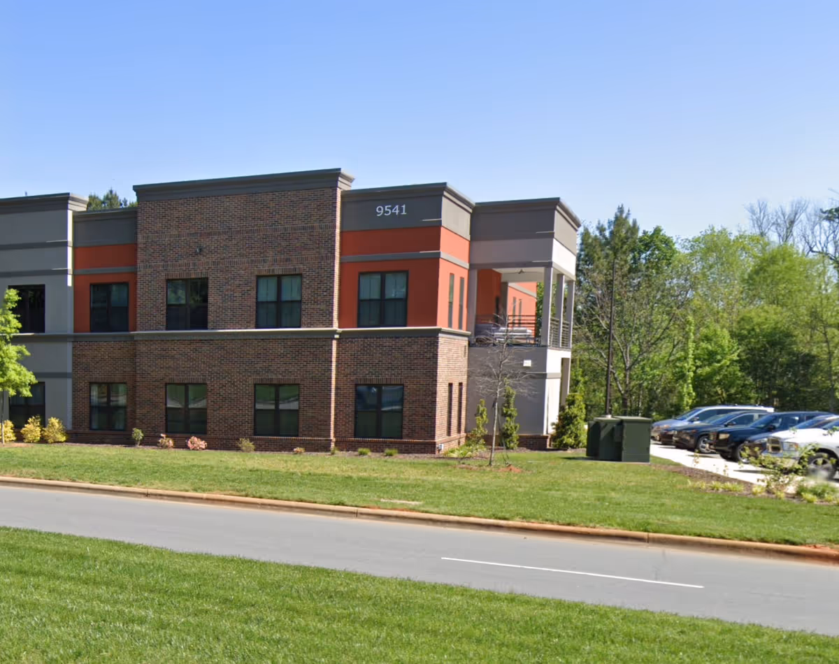 Exterior view of a brick senior living facility with parking and greenery.
