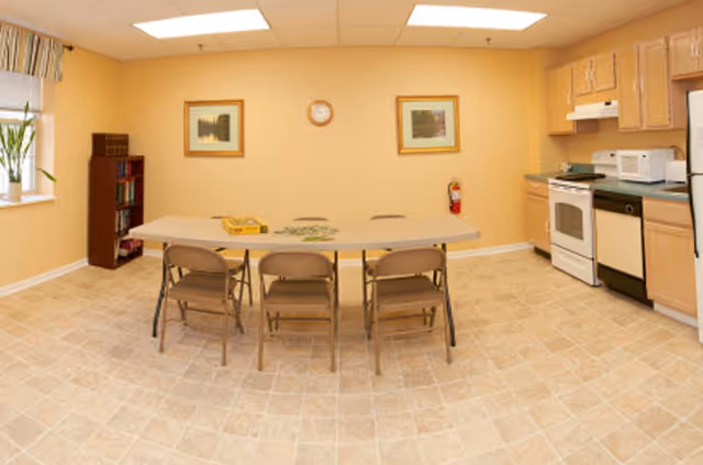 Small communal dining/activity room with a folding table and chairs and a kitchenette along the right wall.
