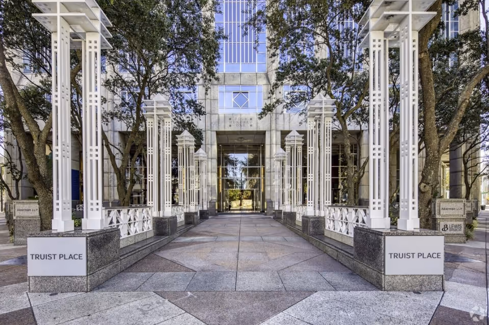 Wide outdoor walkway with white lattice columns leads to a glass-front building entrance.