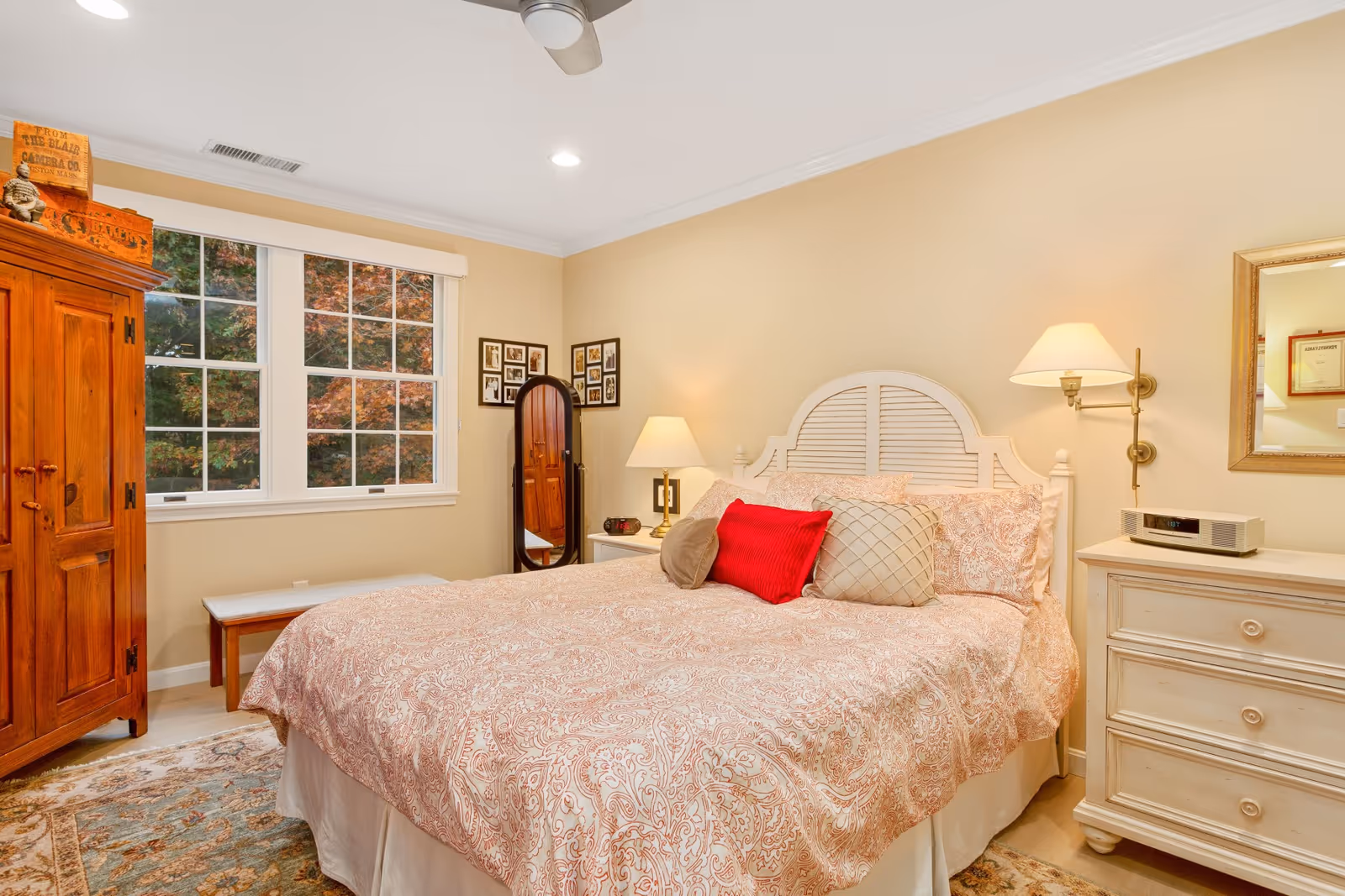 Bright, cozy bedroom featuring a white headboard bed, dresser, and large wooden armoire.