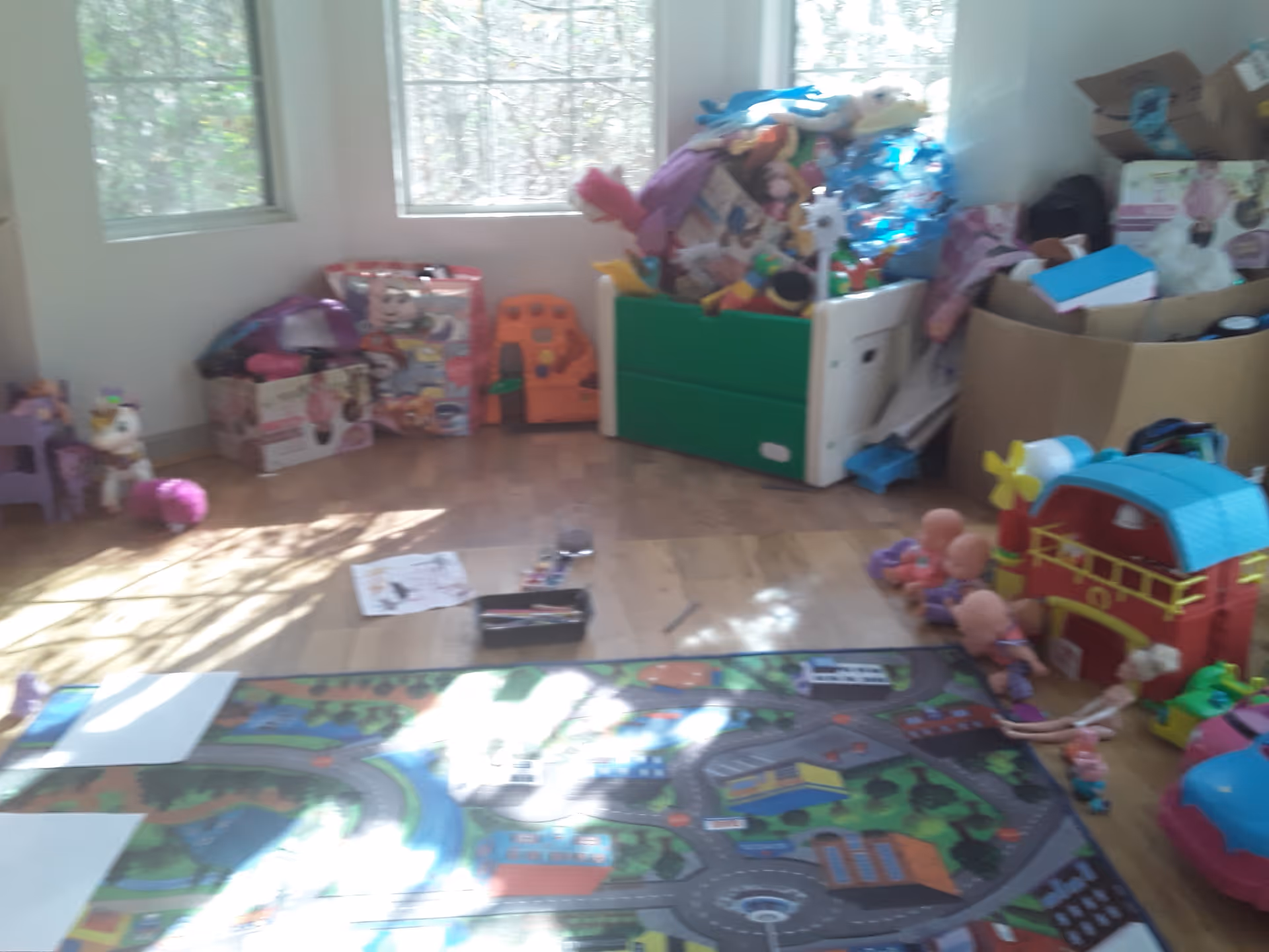 Bright playroom with windows and scattered children's toys, boxes, and a colorful toy barn.