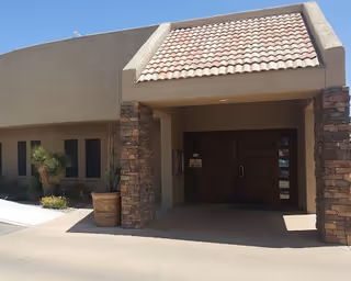 Exterior entrance of Santa Rita Nursing and Rehabilitation Center with stone columns and double wooden doors.