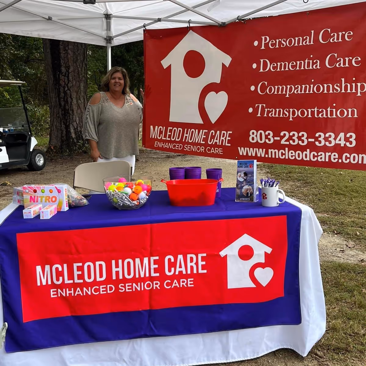 Outdoor promotional booth with McLeod Home Care banner and a smiling woman