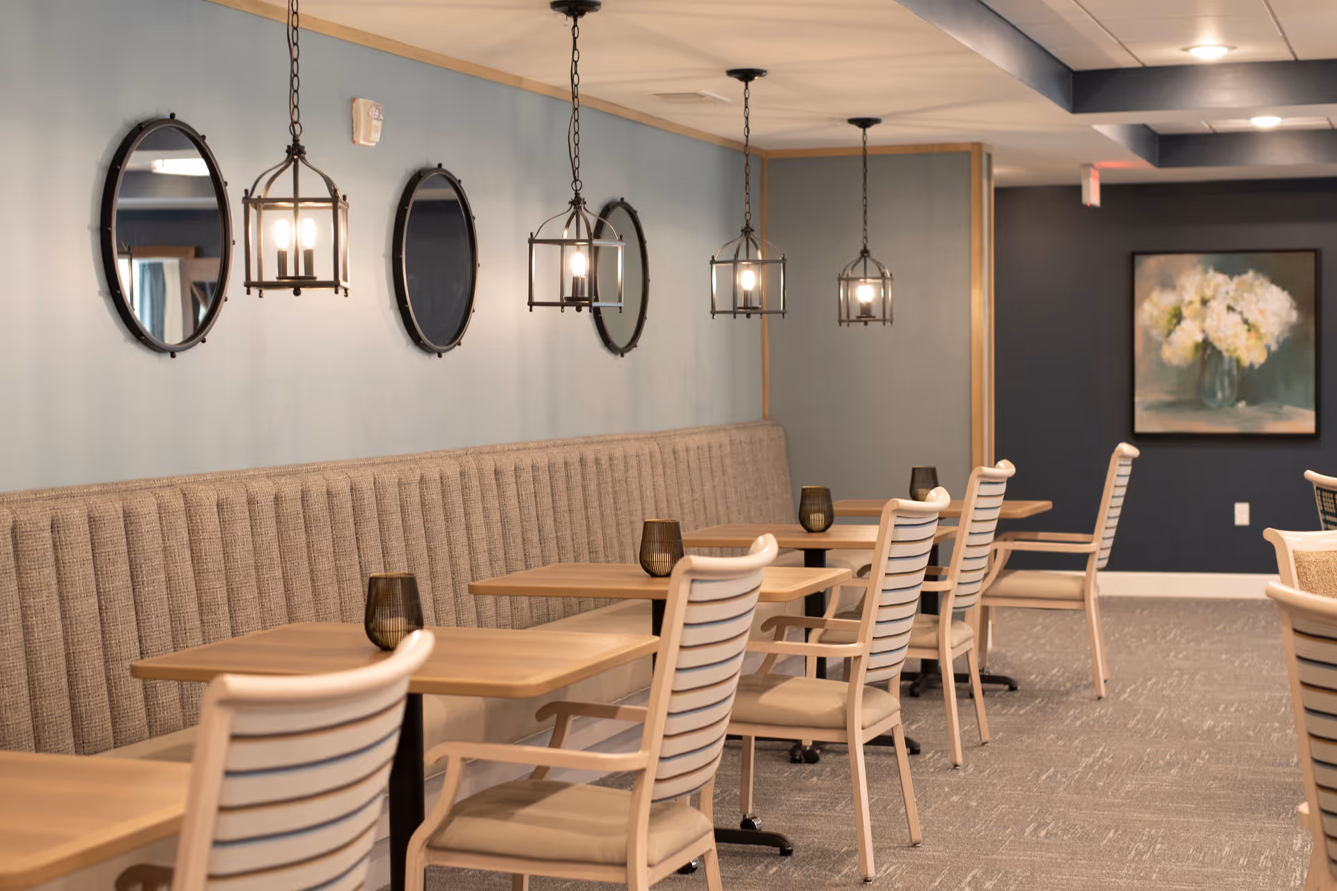 Dining area with beige chairs, wooden tables, pendant lights, and wall-mounted mirrors.