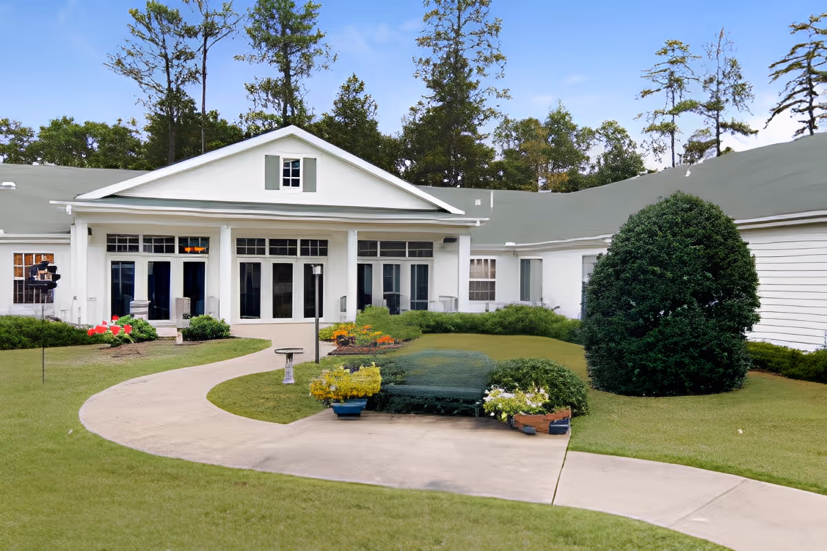 Front exterior of a single-story white building with columns, large windows, a curved walkway, and landscaped lawn and shrubs.