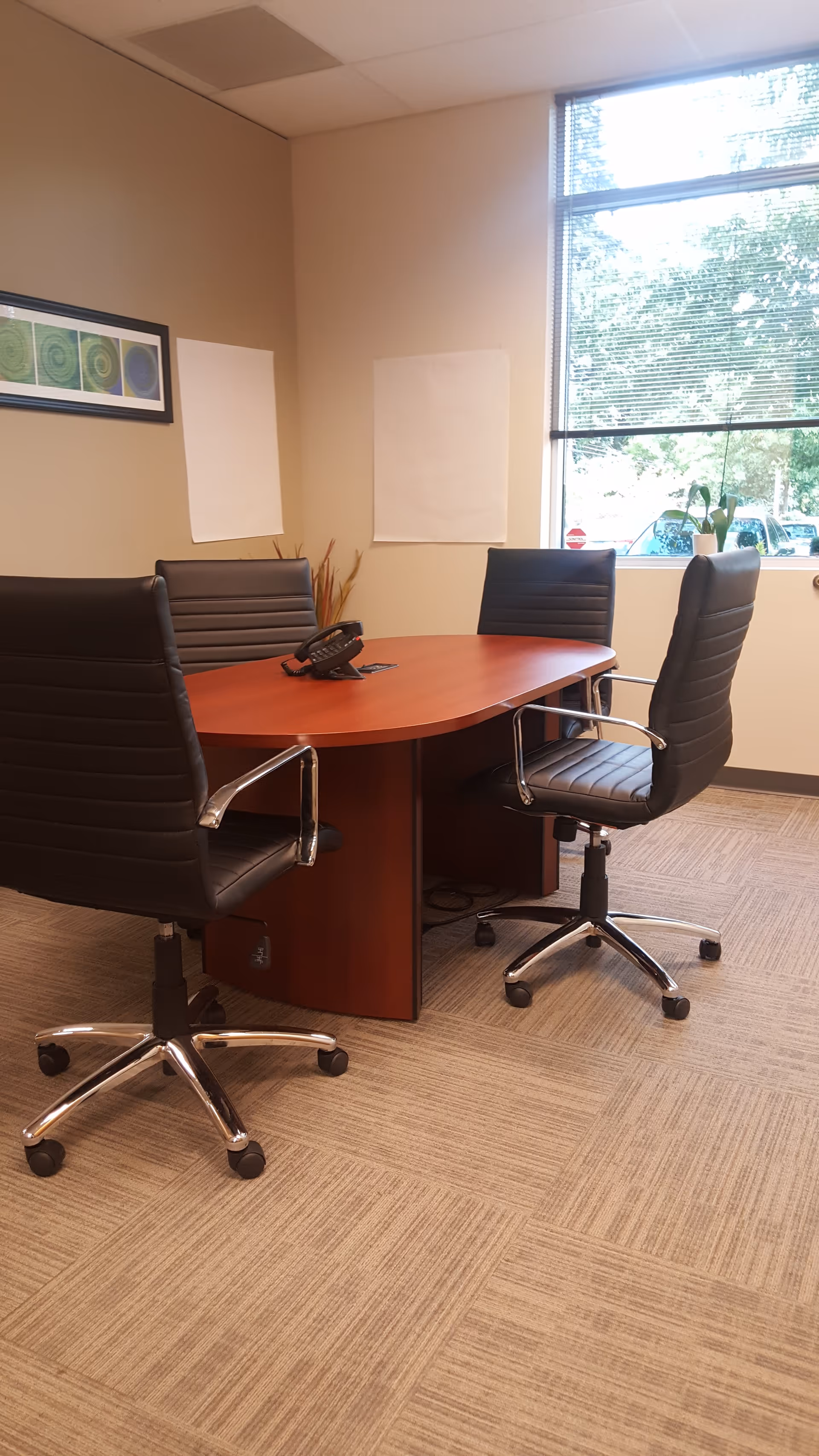 A conference room with a wooden oval table and four black swivel chairs.