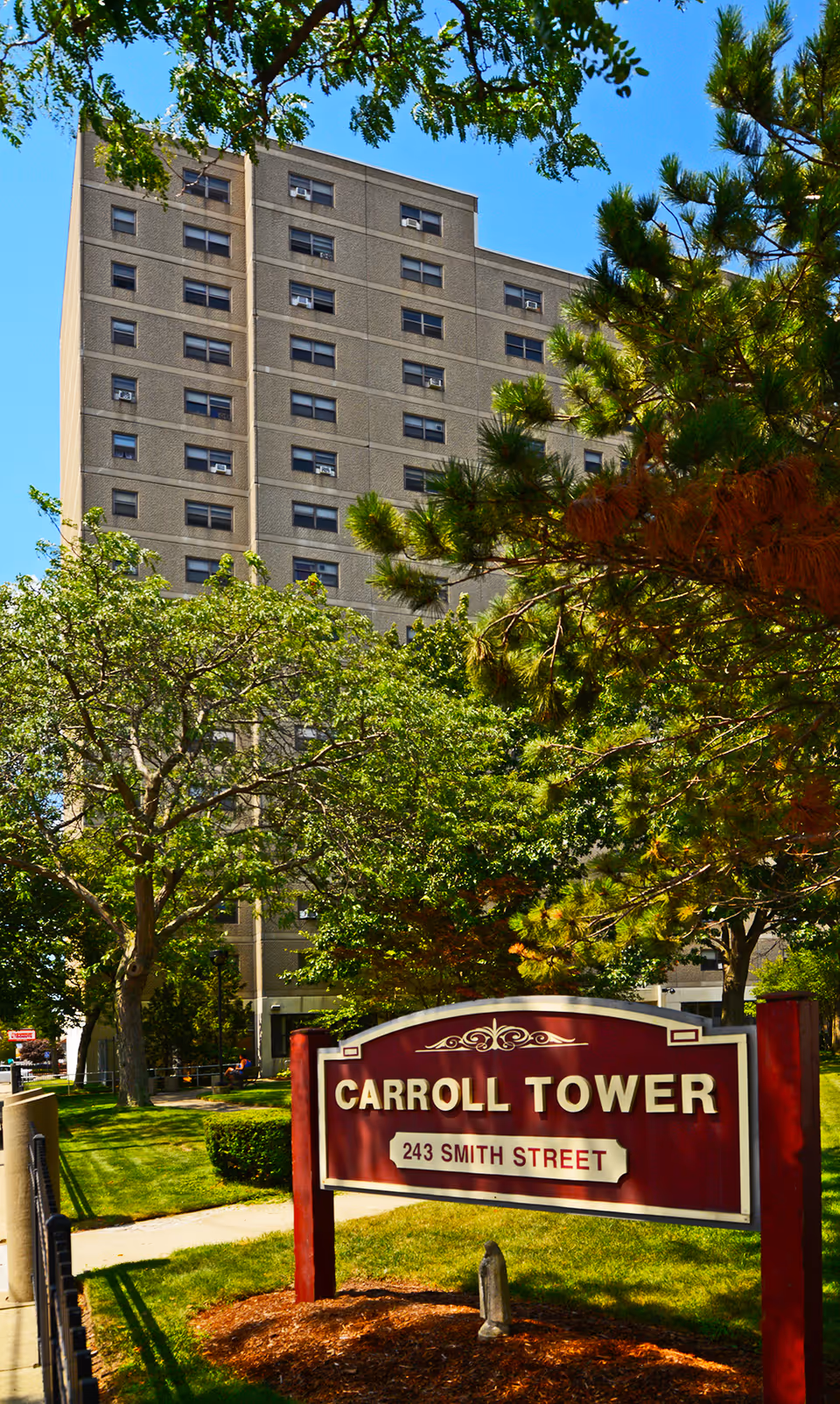 Tall beige senior living building with Carroll Tower sign amid green trees
