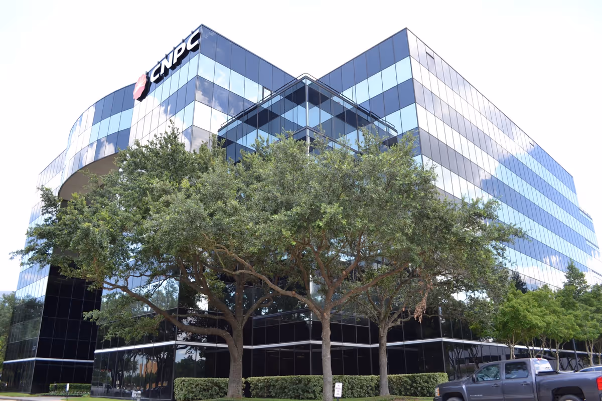 A modern glass office building with trees in the foreground