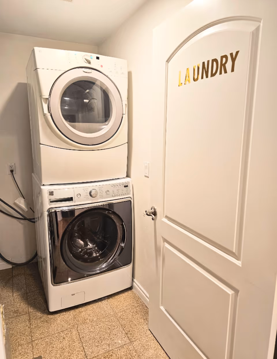 Stacked washer and dryer in a small laundry room beside a labeled door.