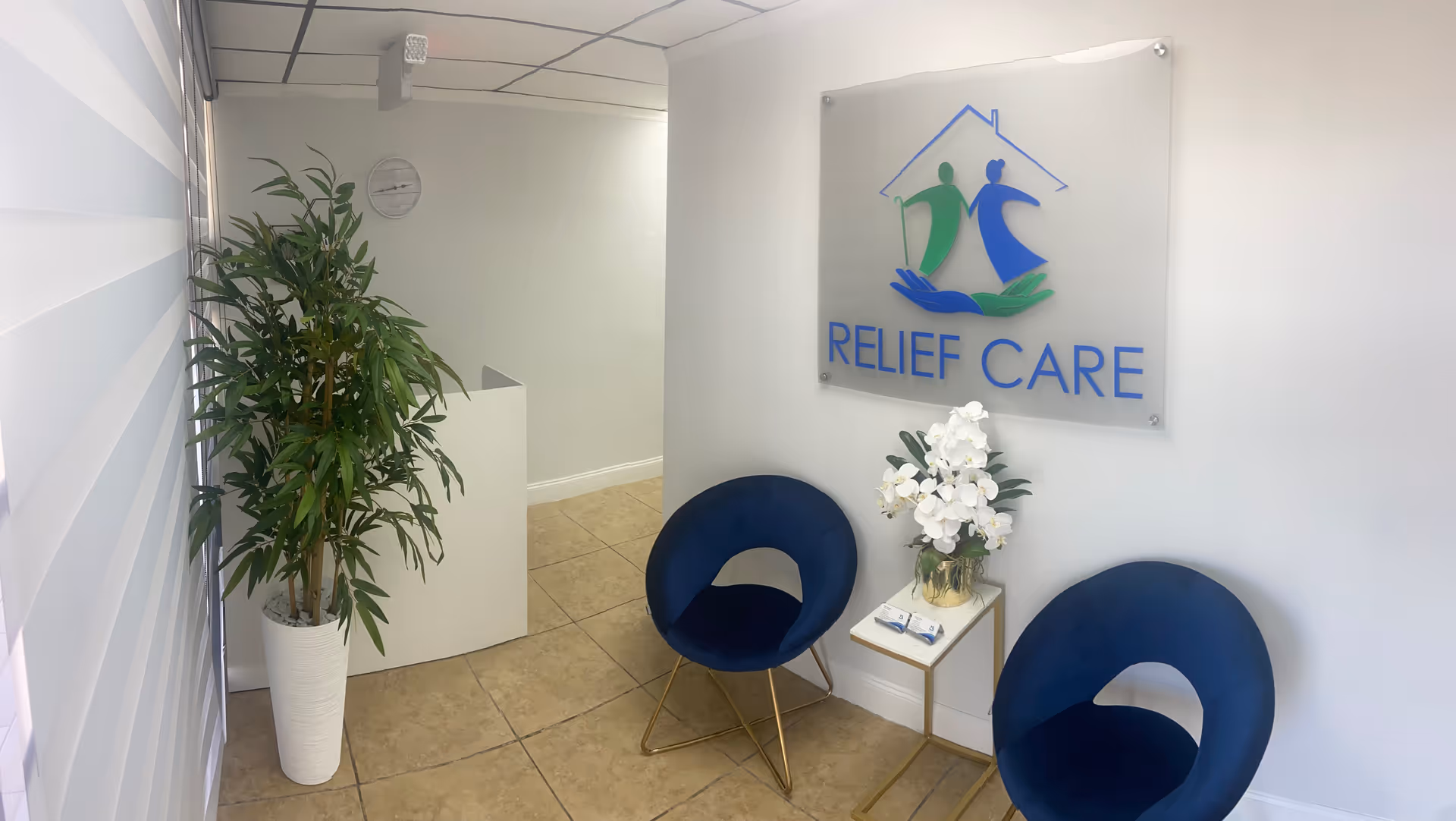 Reception area with Relief Care sign, two blue chairs, plant, and flowers.