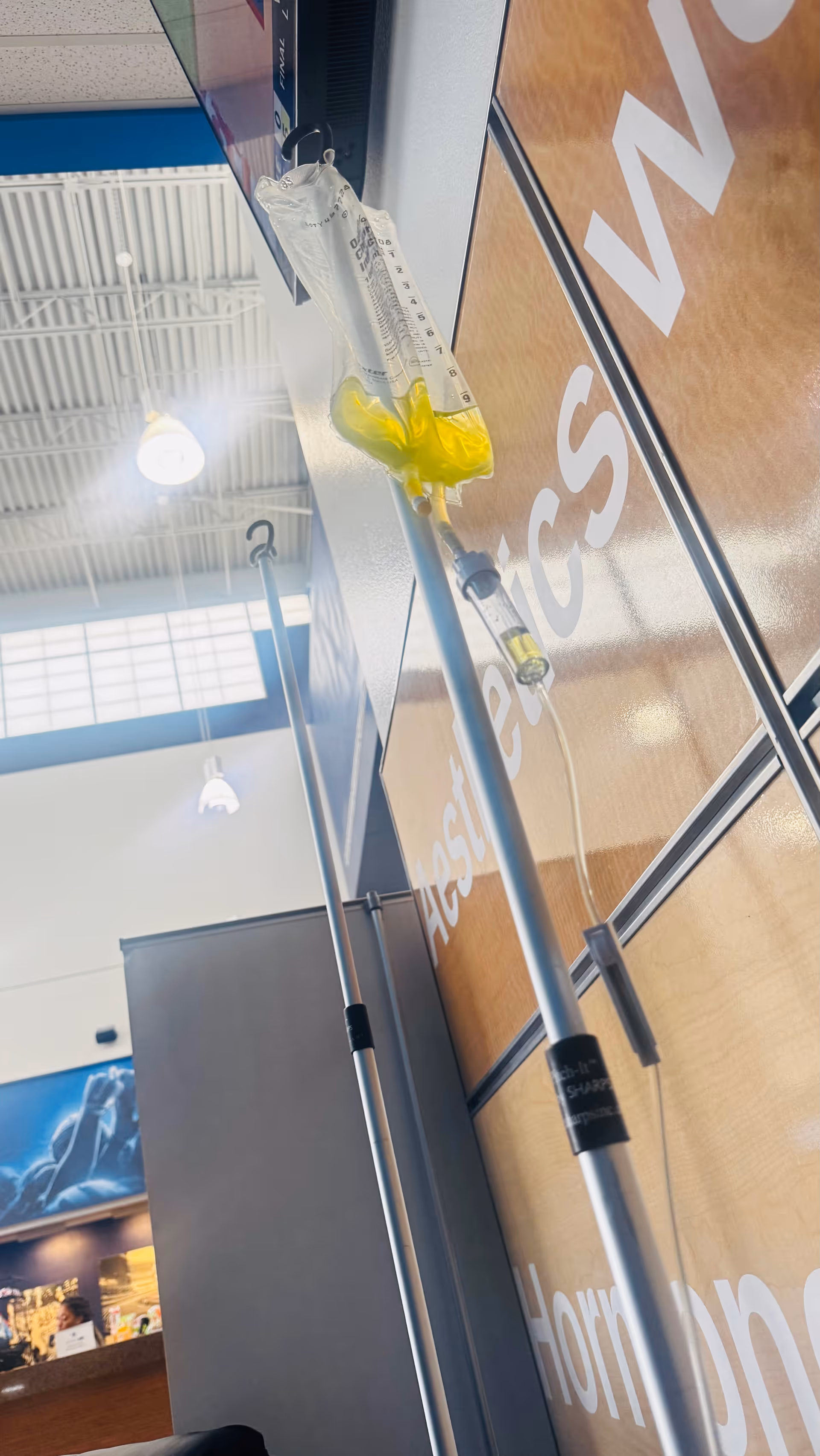 IV bag hanging from a stand inside a clinic, next to a glass wall with signage.