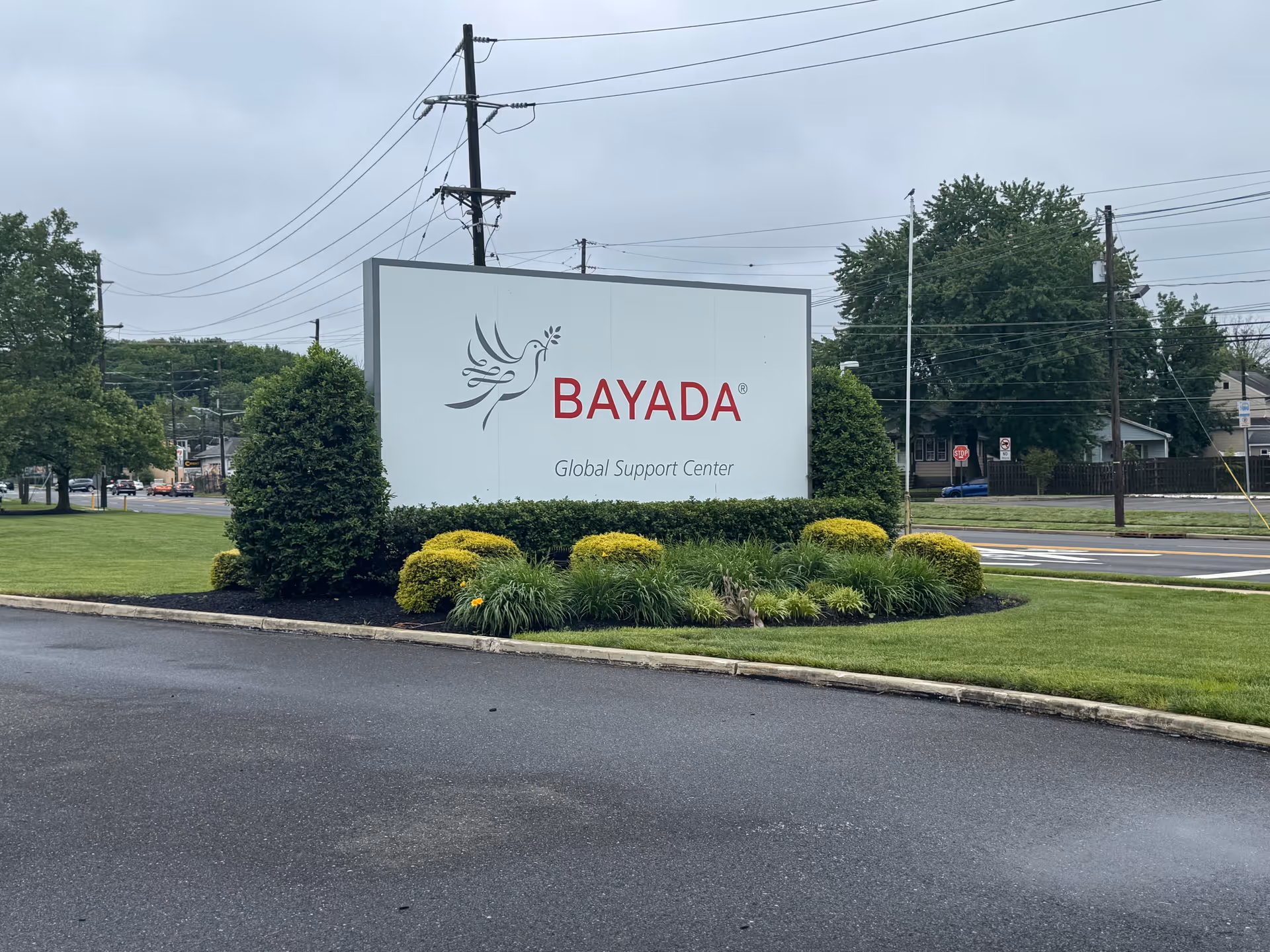 A BAYADA Global Support Center sign amid landscaped bushes beside the road.