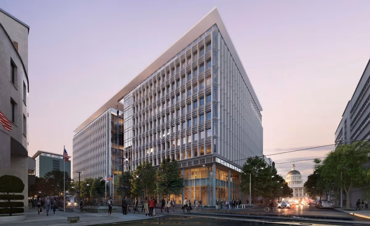 Modern glass-front building with a wide street, trees, and pedestrians at dusk
