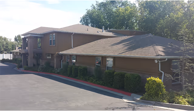 Exterior view of Alta Ridge Assisted Living of Holladay, a brown single-story building with shrubs.