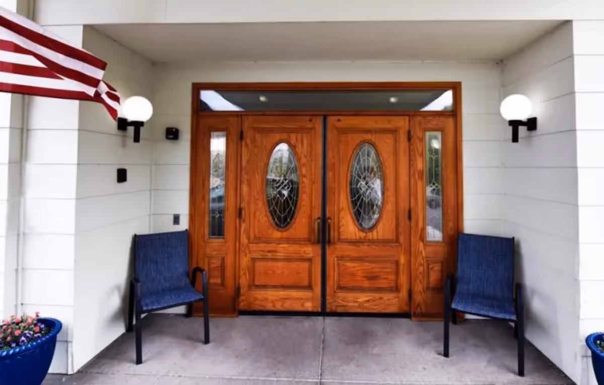 Two blue chairs flank wooden doors at Regency Village entrance.