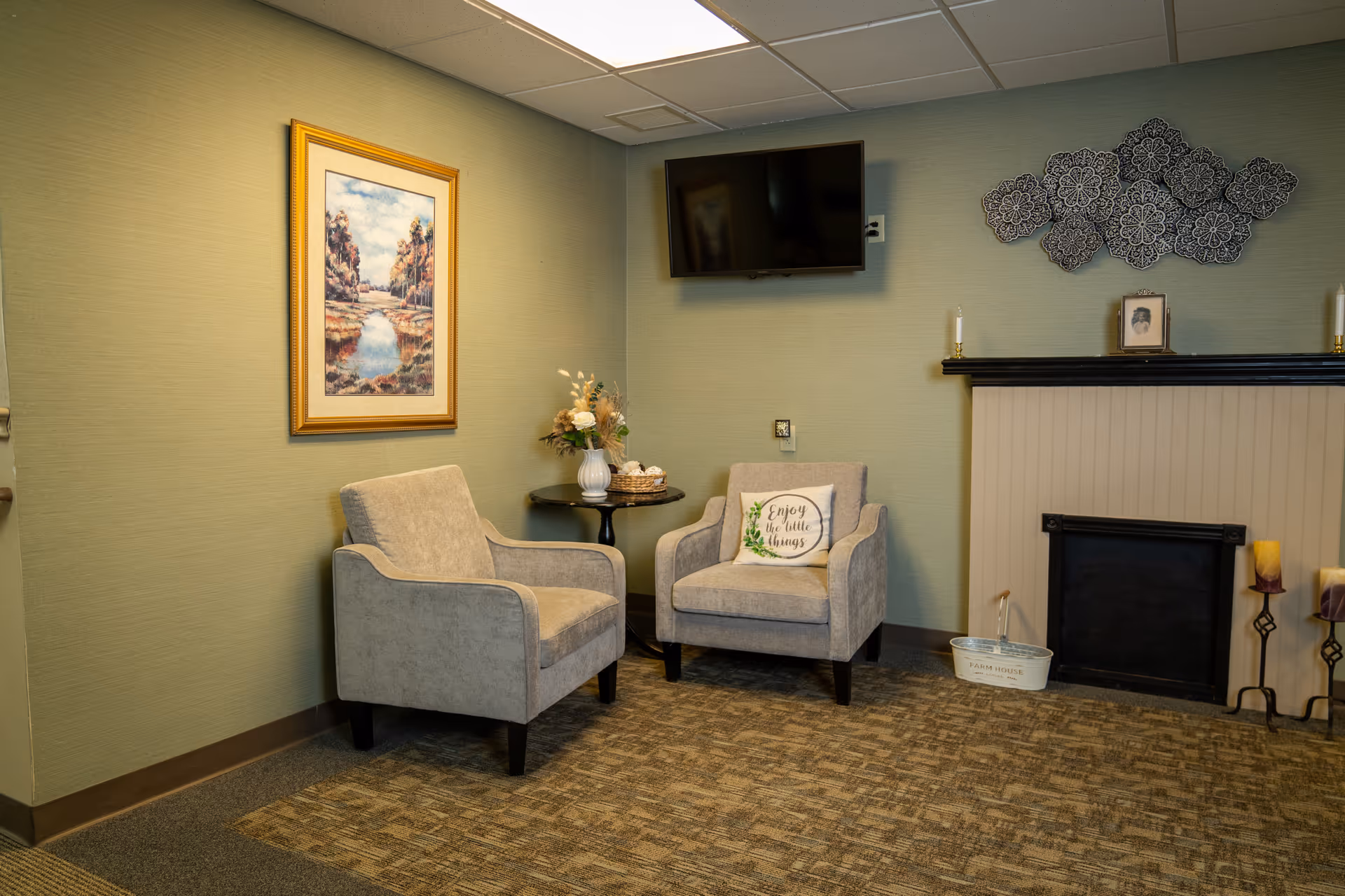 Two gray armchairs around a round table in a cozy living room with a fireplace.