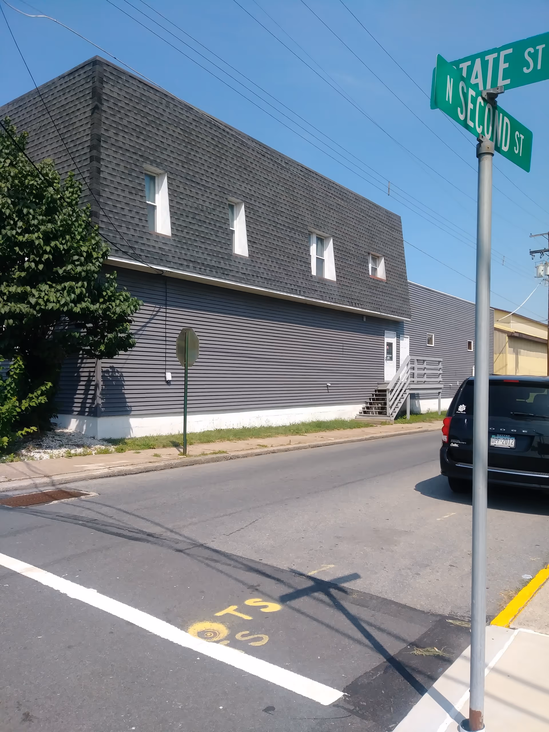 Exterior view of a gray, two-story building along a street with a car and street signs.