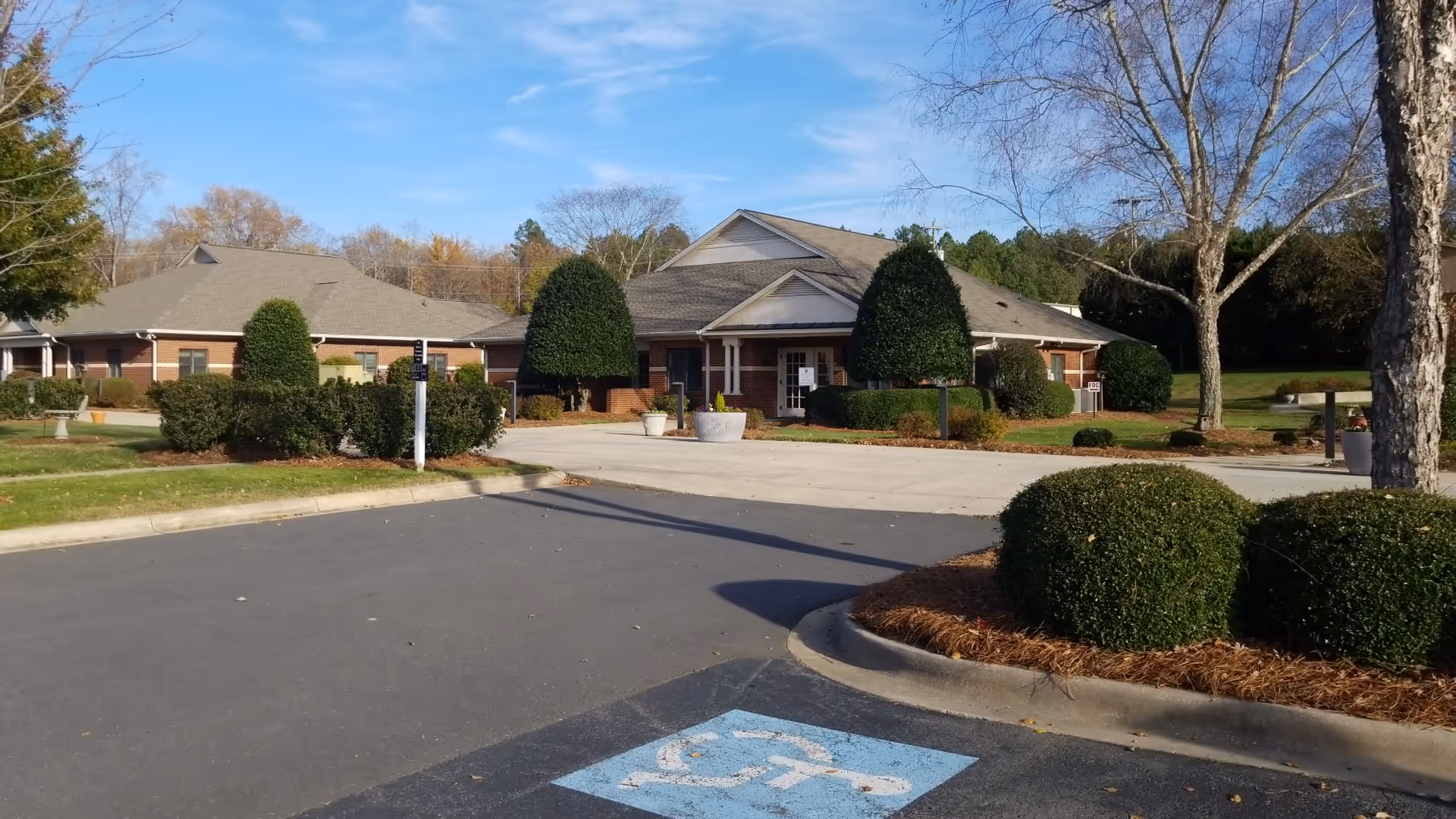 Exterior view of a single-story senior living facility with manicured shrubs and driveway.