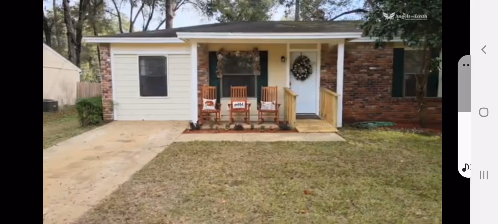 A small residential brick-and-siding house with a front porch and three wooden rocking chairs.