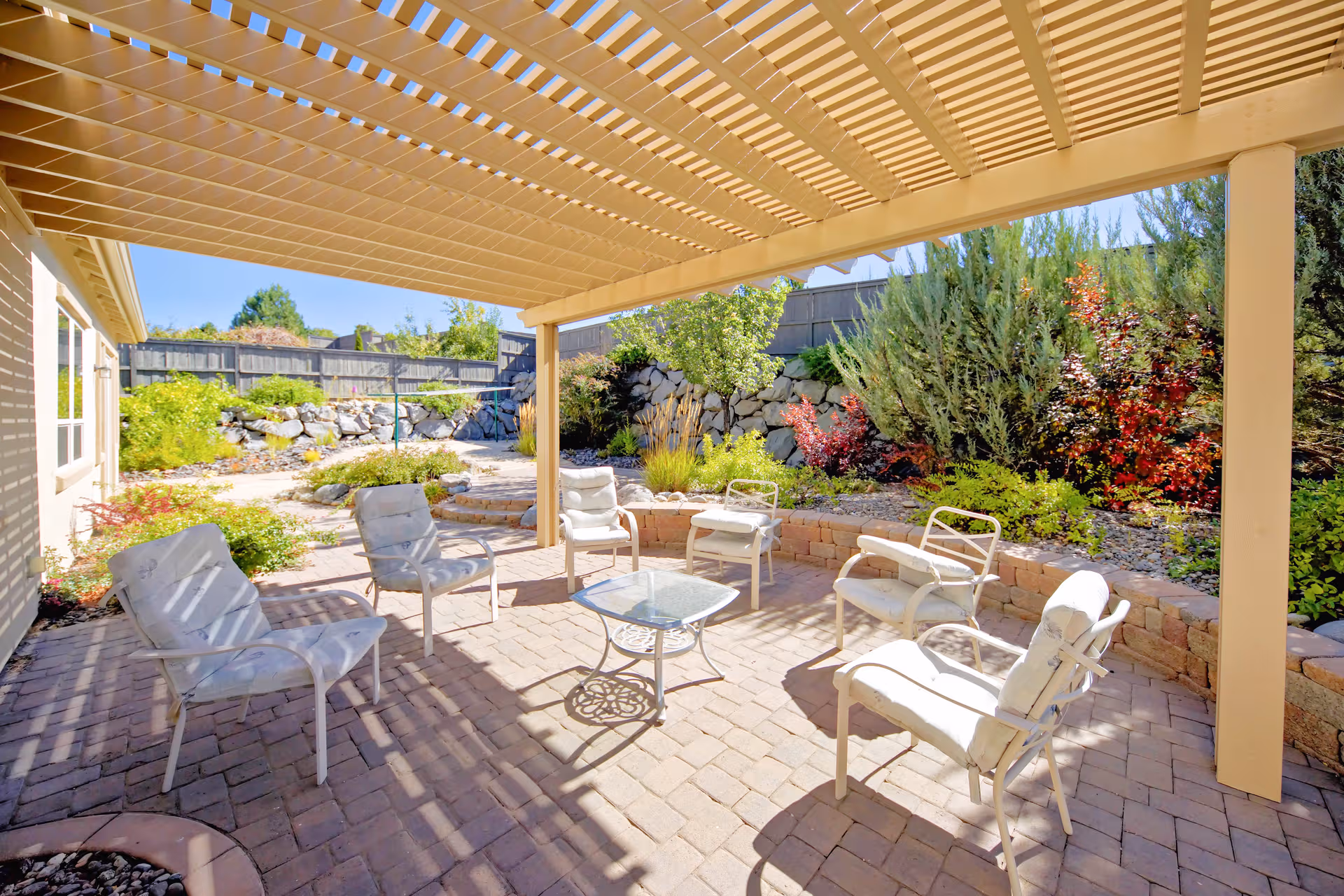 Sunny outdoor patio with white chairs arranged around a glass table under a pergola.