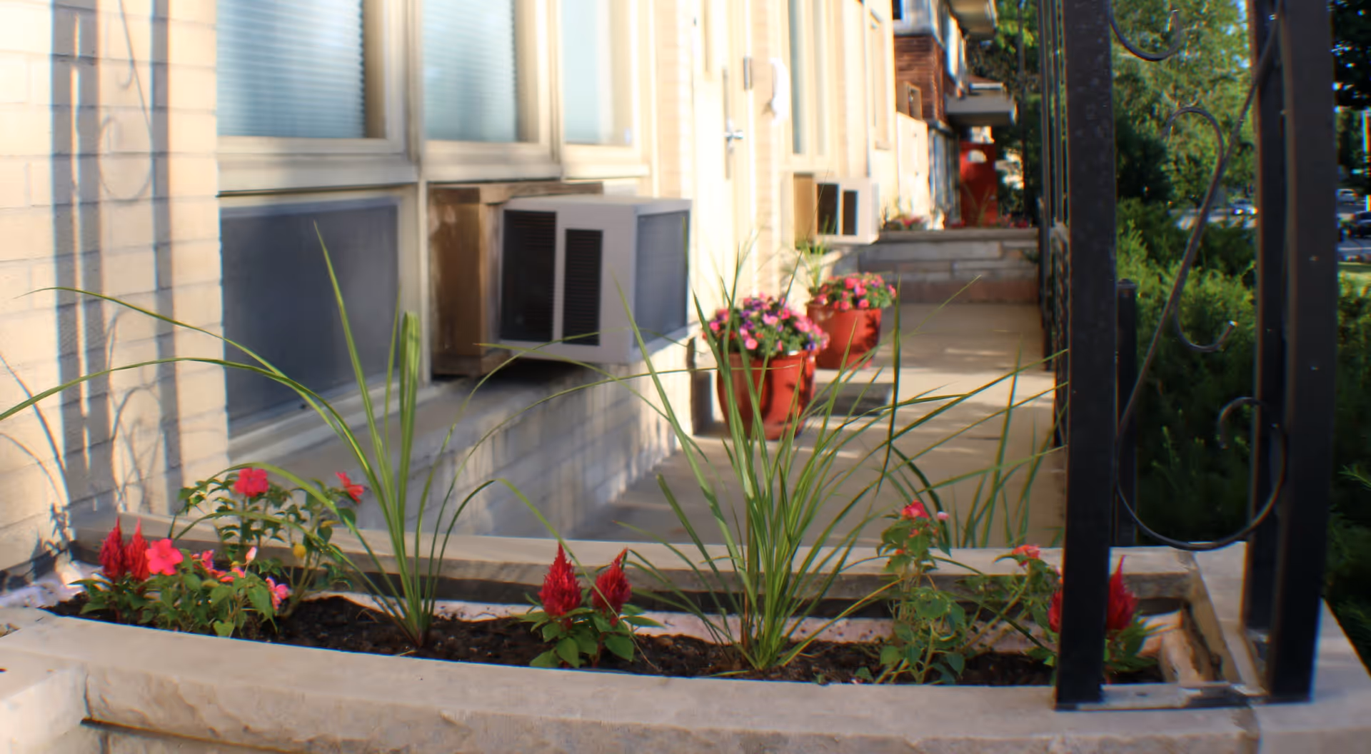 Exterior walkway with planter boxes, colorful flowers, and a railing along the building.