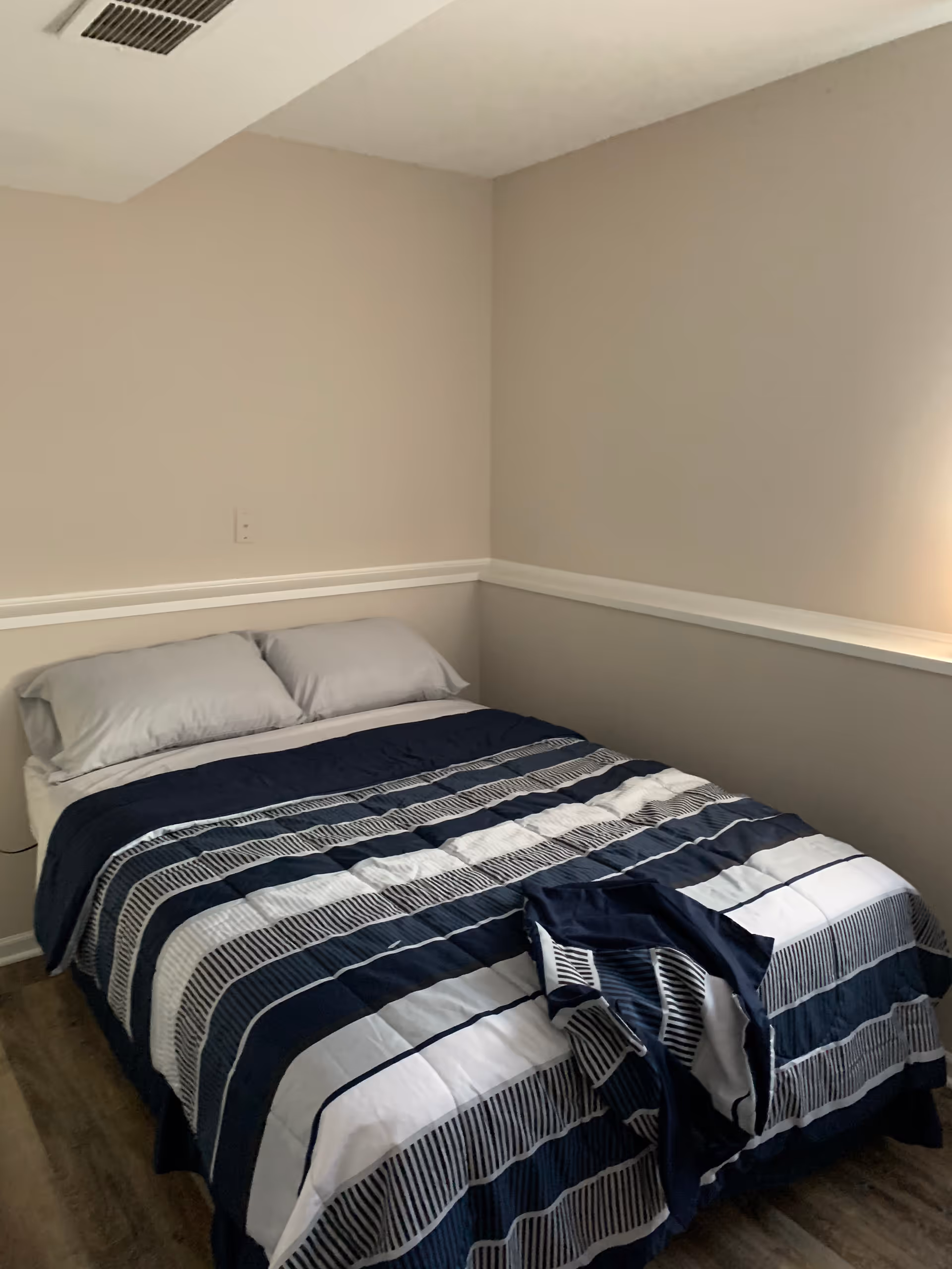 Cozy bedroom with striped bedding and neutral walls in a senior living facility.