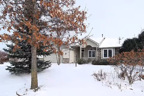 Snow-covered front of a senior living facility with trees and shrubs.