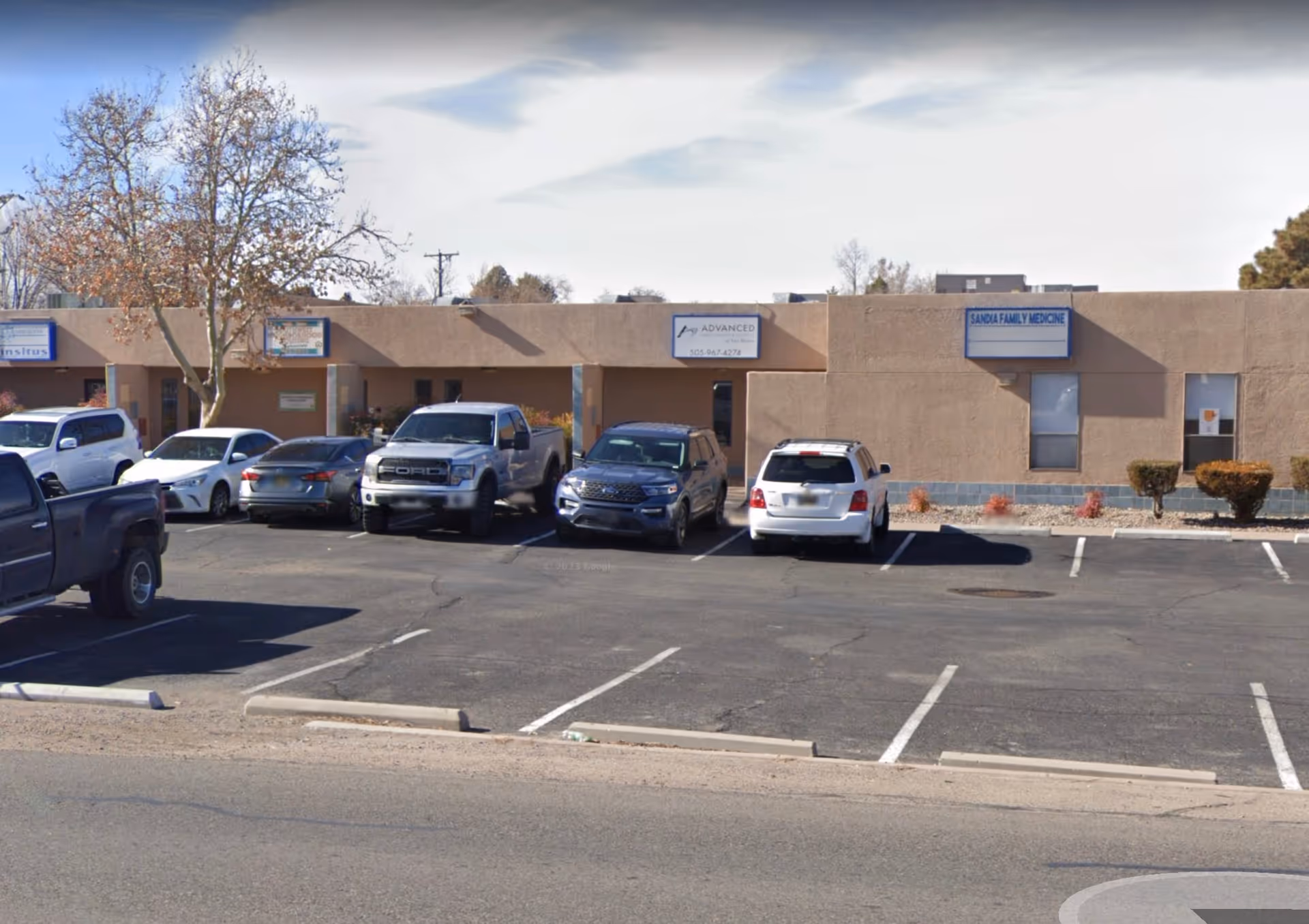 Exterior beige medical building with a parking lot and cars in front.
