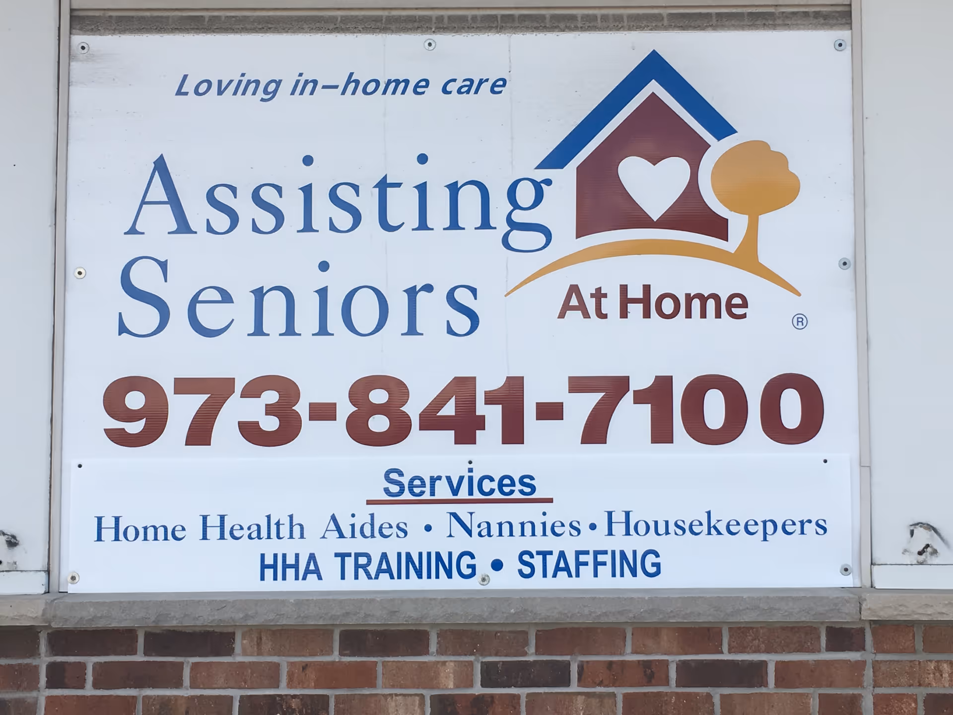 Exterior sign for Assisting Seniors At Home displaying contact number and services.