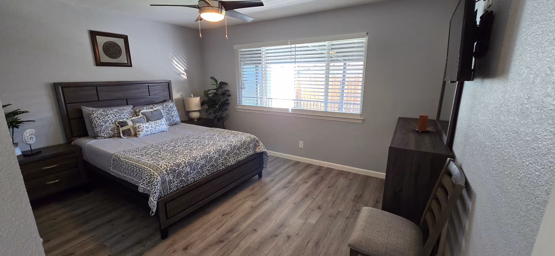 A clean, modern bedroom in a senior living facility with a bed, nightstands, dresser, and window.