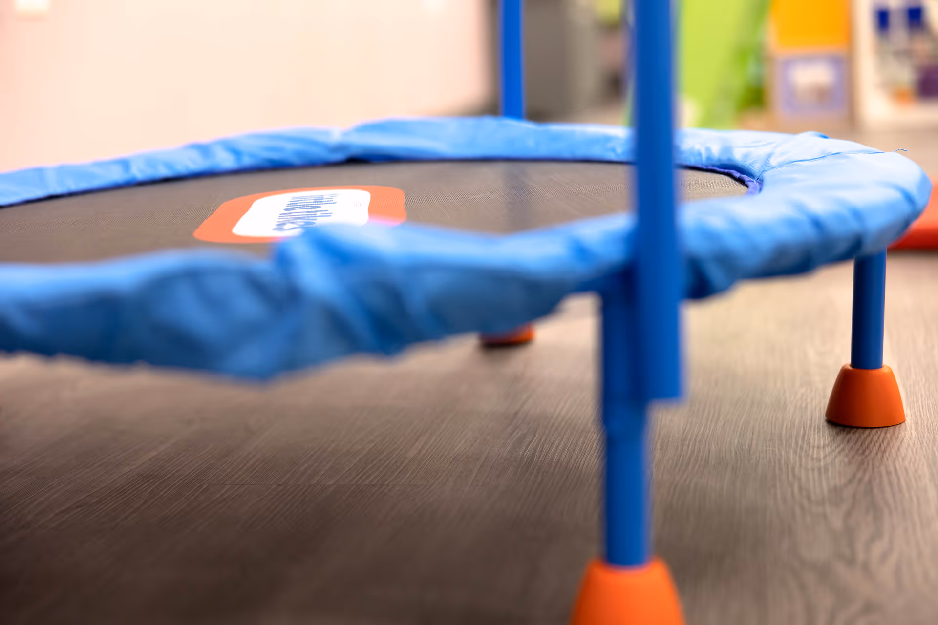 Close-up of a small blue trampoline with orange feet indoors.