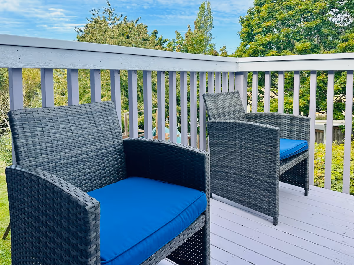 Two wicker outdoor chairs with blue cushions on a wooden balcony overlooking trees.