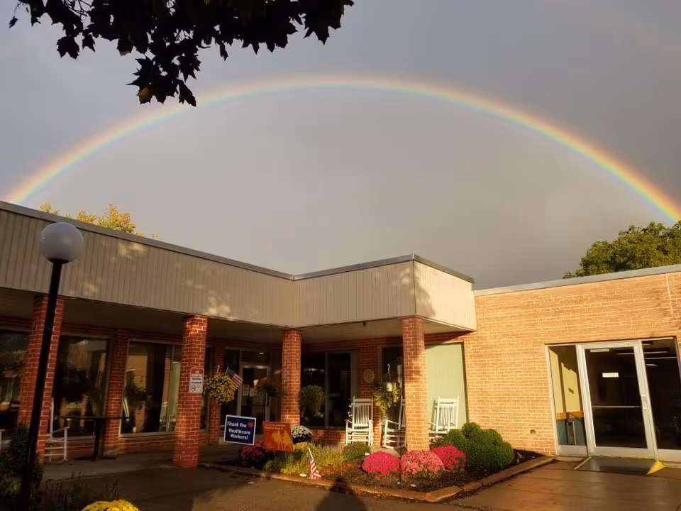 Exterior view of Leroy Village Green shows brick building and double rainbow over entrance.