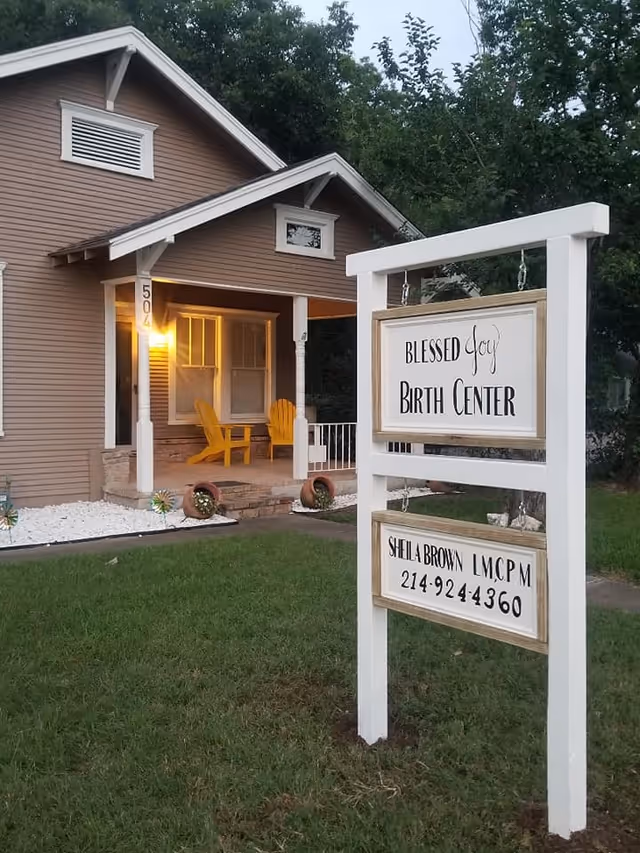Front exterior of Blessed Joy Birth Center with sign and yellow chairs on porch