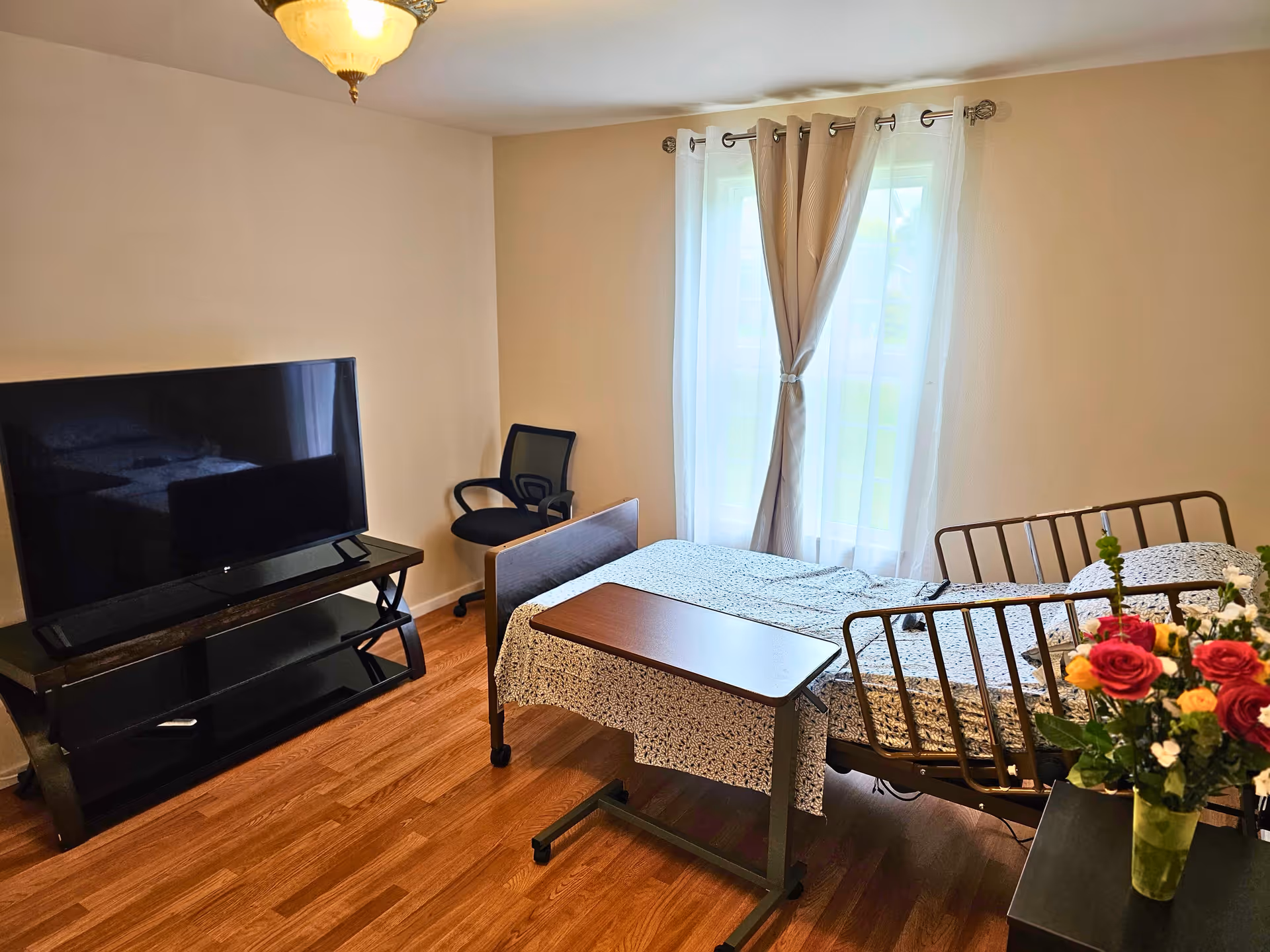 A furnished senior living bedroom with two metal-framed beds, a TV, and a window.