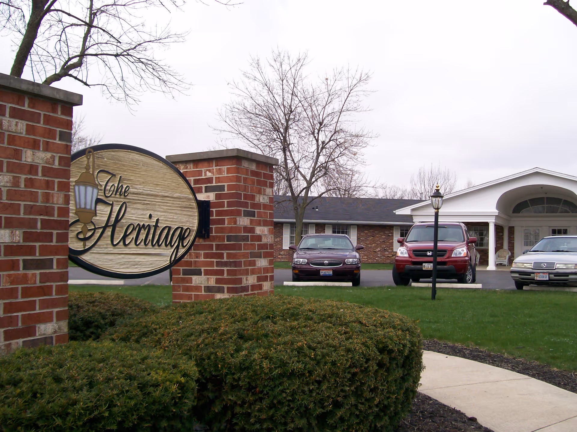 Exterior view of The Heritage facility with brick sign pillars, parking lot, and front entrance.