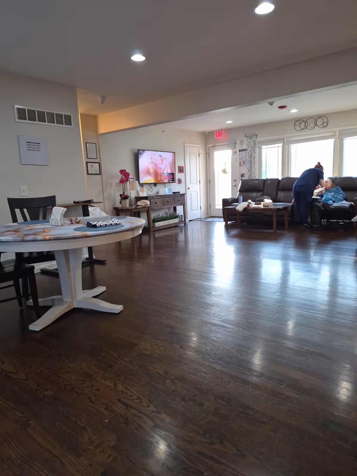 Senior living common area with dining table, TV, and residents on couches