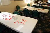 Two white tables with scattered red petals and green chairs in a dining room.
